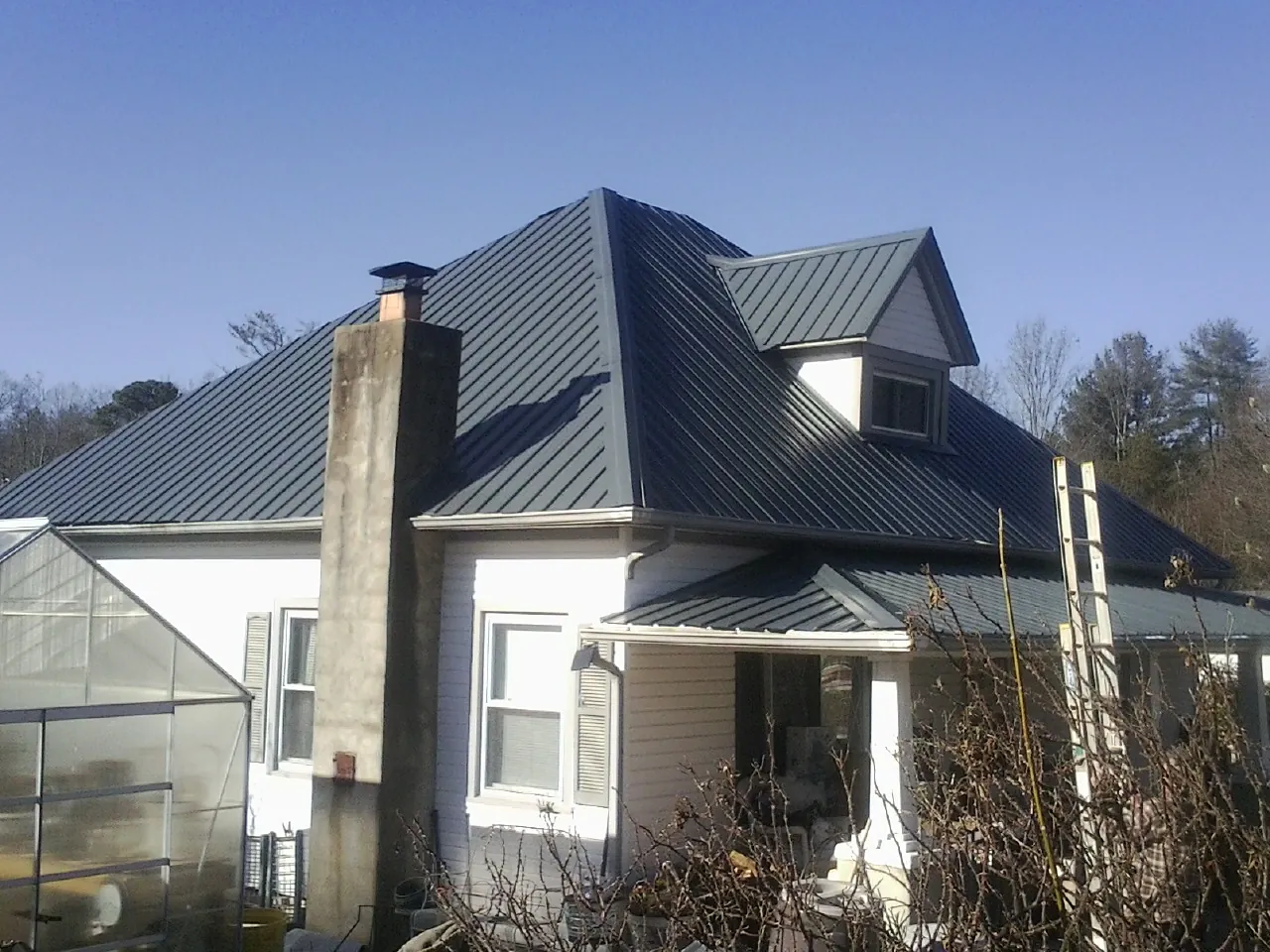 Dark blue standing seam metal roof on a white farmhouse with dormer — Slate & Tile Roof Repair by Roofing Brothers in Wray