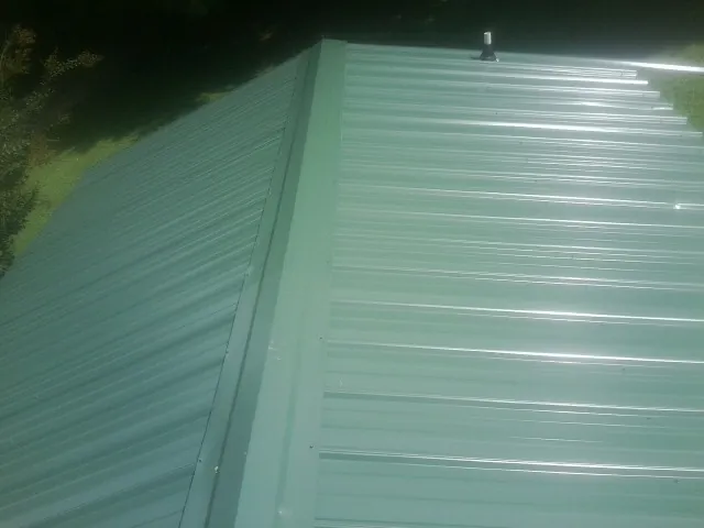 New green metal panels meeting at the ridge of a roof — Flat Roof Repair work by our crew in Wray