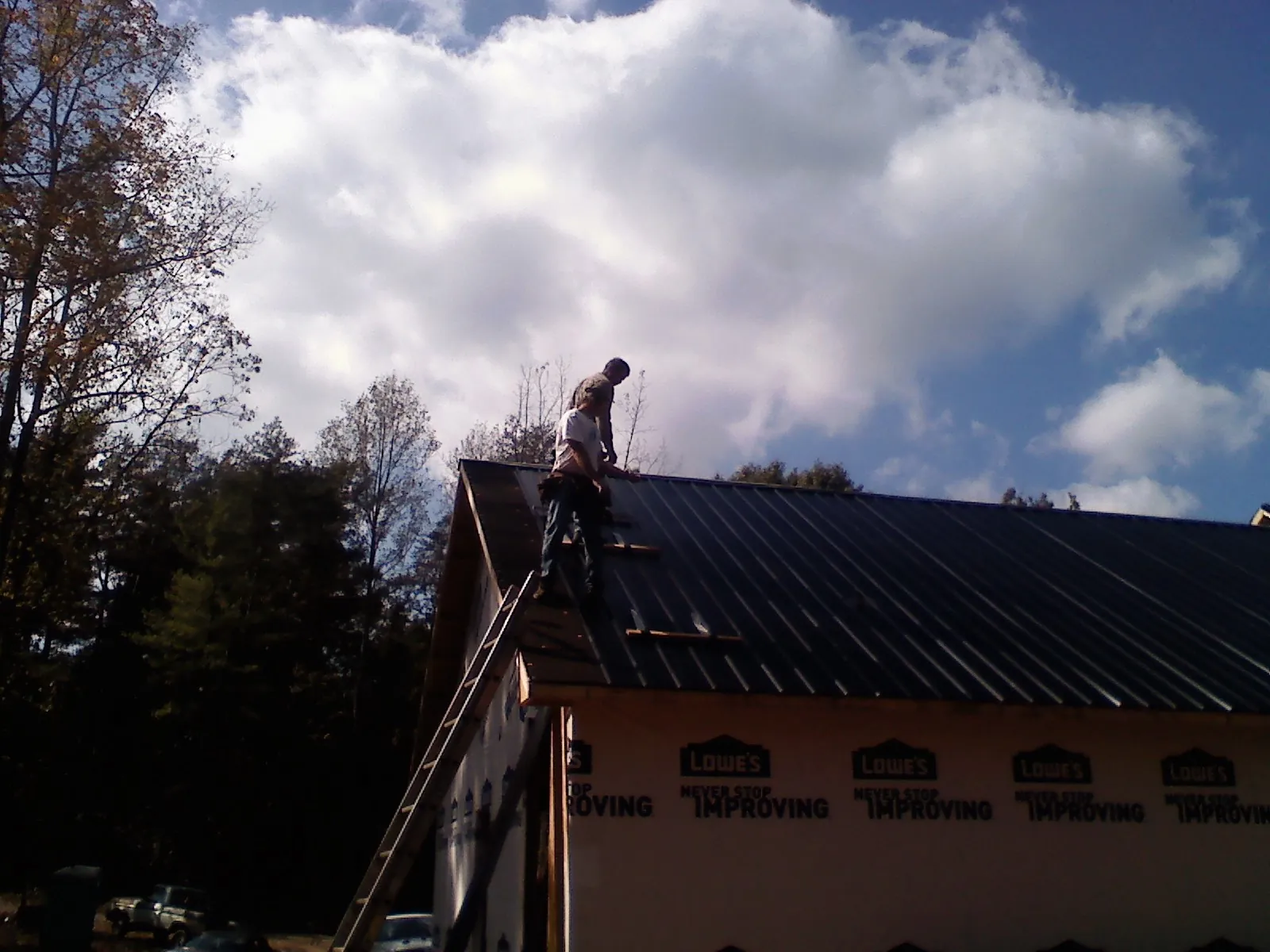 Roofer fastening dark metal panels high against a cloudy sky, from a Roof Inspection job in Wray