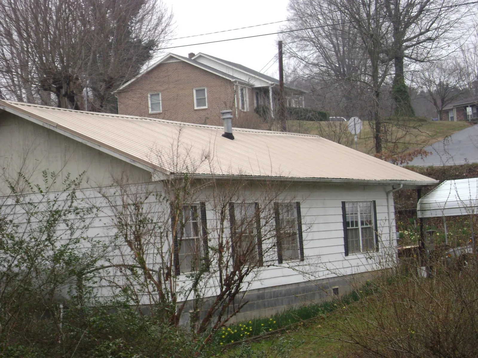 Tan metal roof on a white sided house set into a hillside — Commercial Roofing by Roofing Brothers in Wray