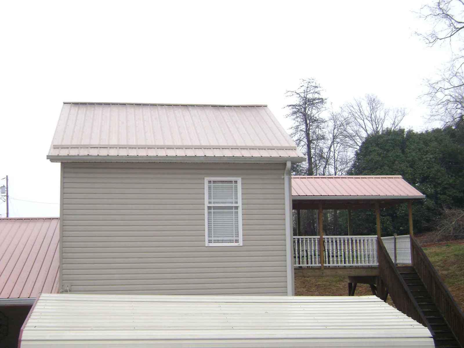 Tan metal roofs on a two story addition and attached porch, from a Roof Replacement job in Wray